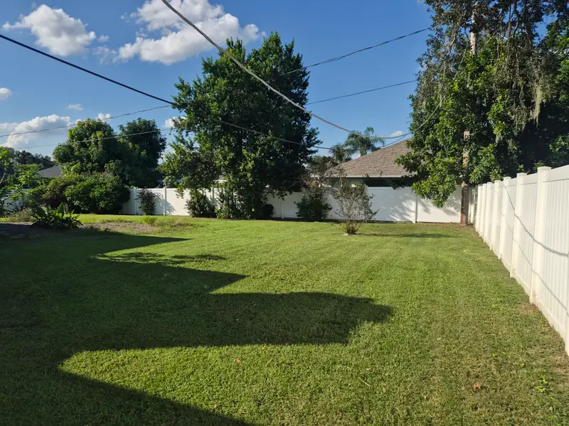 A freshly mowed backyard with clean stripes along a white vinyl fence, mowed by LoLo Lawncare in the Tampa area