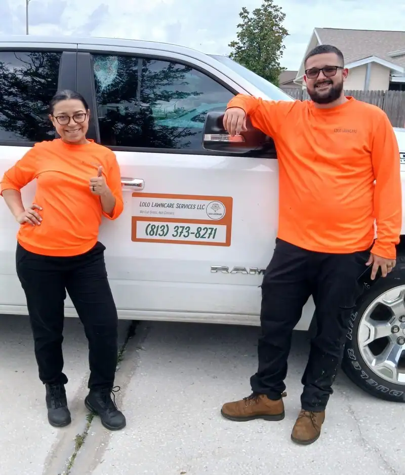 The husband-and-wife team behind LoLo Lawncare in orange company shirts beside their truck